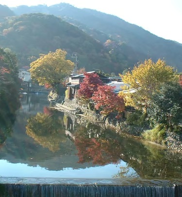 Autumn trees and a pavilion reflected in calm water in Arashiyama