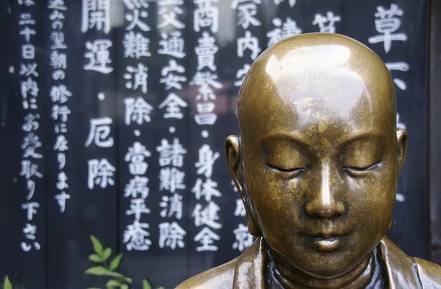 A golden Buddha head in front of a wall of Japanese inscriptions