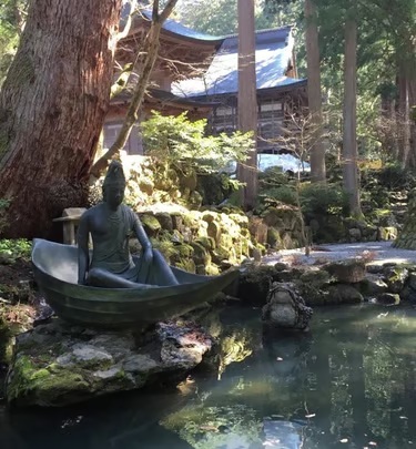 A seated statue beside a pond and temple buildings in Japan